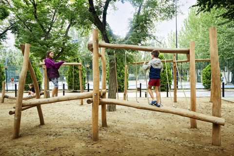 Des enfants jouent sur une aire de jeux en bois dans un site de glamping entouré d’arbres.