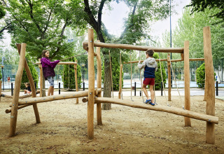 Des enfants jouent sur une aire de jeux en bois dans un site de glamping entouré d’arbres.