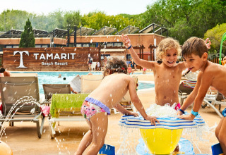 Kinderen spelen bij een waterspeeltoestel in Tamarit Beach Resort in Spanje, zwembad en ligstoelen op de achtergrond.