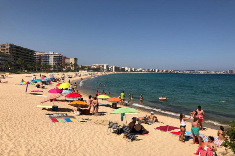Strandscene ved Camping Interpals- Bungalow Sa Riera i Spanien med folk, farverige parasoller og havudsigt.