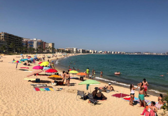 Strandtafereel aan Camping Interpals- Bungalow Sa Riera in Spanje met mensen, parasols en zicht op zee.