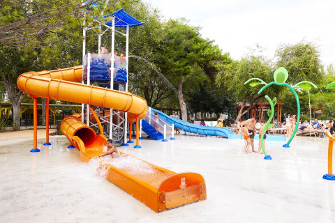 Des enfants jouent sur des toboggans orange et bleu dans un parc aquatique extérieur d’un hébergement glamping.