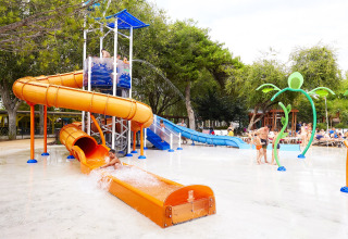 Des enfants jouent sur des toboggans orange et bleu dans un parc aquatique extérieur d’un hébergement glamping.