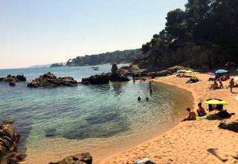 Plage du CAMPING INTERPALS- Bungalow Sa Riera en Espagne, sable doré, rochers et vacanciers à la baignade.