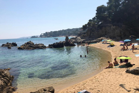 Udsigt over stranden ved CAMPING INTERPALS- Bungalow Sa Riera i Spanien med klipper, sand og badegæster.