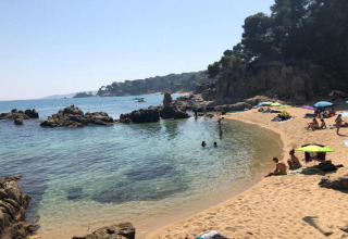 Udsigt over stranden ved CAMPING INTERPALS- Bungalow Sa Riera i Spanien med klipper, sand og badegæster.