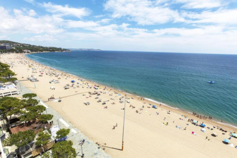 Strandudsigt fra CAMPING INTERPALS - Bungalow Sa Riera i Spanien med blå himmel, hav og solbadende gæster.