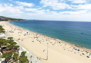 Strandudsigt fra CAMPING INTERPALS - Bungalow Sa Riera i Spanien med blå himmel, hav og solbadende gæster.