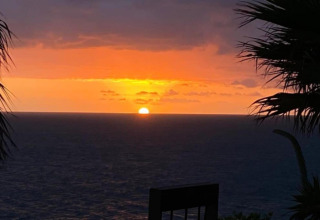 Zonsondergang boven zee vanaf Tamarit Park Resort 1 THALASSA in Spanje, met palmbomen op de voorgrond.
