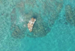 Luftfoto af klart blåt vand og en sten midt i havet nær Tamarit Park Resort 1 THALASSA i Spanien.