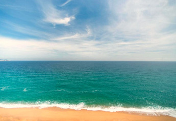 Vue sur la mer turquoise et la plage de sable sous un ciel bleu au CAMPING INTERPALS, Sa Riera, Espagne.