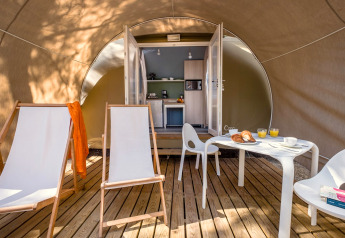 Vue intérieure d’une tente safari avec terrasse en bois, chaises longues et coin cuisine au Camping Estival Torre de la Mora en Espagne.