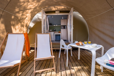 Inde i en safari-telt med træterrasse, loungestole, bord og moderne tekøkken ved Camping Estival Torre de la Mora i Spanien.