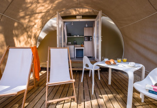 Inde i en safari-telt med træterrasse, loungestole, bord og moderne tekøkken ved Camping Estival Torre de la Mora i Spanien.