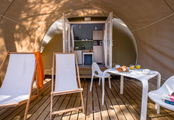 Blick in ein Safari-Zelt mit Holzterrasse, Liegestühlen, Tisch und Küche im Camping Estival Torre de la Mora in Spanien.