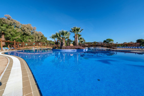 Piscina all'aperto con palme, ponti in legno e lettini al Camping Estival Torre de la Mora in Spagna.