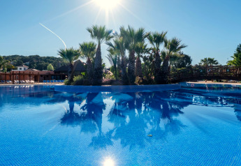 Piscine extérieure avec palmiers et soleil dans un hébergement glamping, entourée de chaises longues et d'un pont.