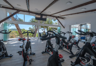 Moderne fitnessrum med spinningcykler og store vinduer med udsigt over naturen på et glampingsted.