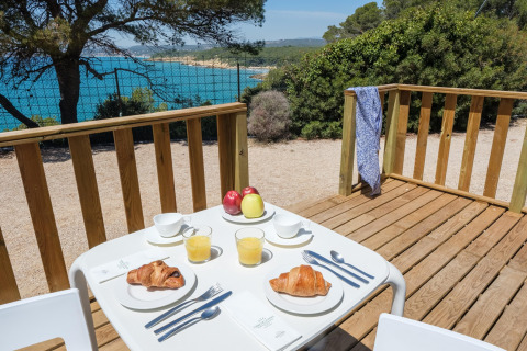 Udendørs morgenmad med croissanter og juice på terrasse med udsigt over havet ved en glampingplads.