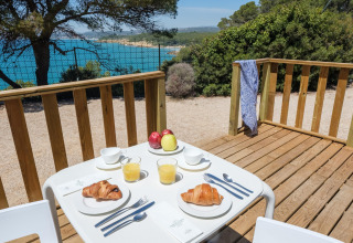 Udendørs morgenmad med croissanter og juice på terrasse med udsigt over havet ved en glampingplads.