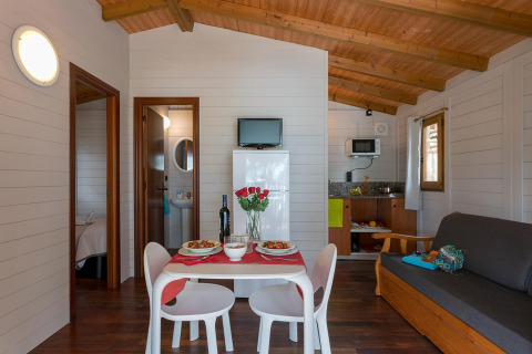 Træbungalow-interiør med spisebord, sofa og køkken i Camping Estival Torre de la Mora, Spanien.