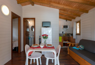 Træbungalow-interiør med spisebord, sofa og køkken i Camping Estival Torre de la Mora, Spanien.