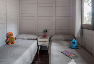 Zwei Betten in einem gemütlichen Holzbungalow mit Plüschtieren, Spielzeug und Buch am Fenster.