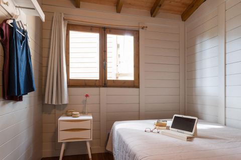 Camera bungalow in legno con letto, finestra, comodino e abiti appesi a Torre de la Mora, Spagna.