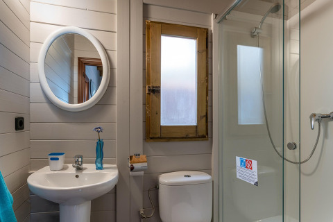 Moderne badeværelse i træhytte med rund spejl, håndvask, toilet og brusedør, camping i Spanien.