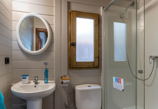 Bagno moderno in bungalow di legno con specchio rotondo, lavabo, WC e doccia in un campeggio in Spagna.