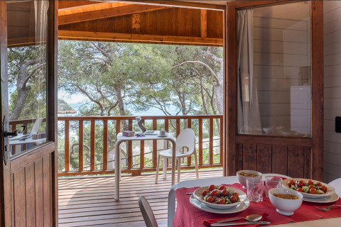 Houten bungalow met zicht op zee en terras, eettafel met maaltijd bij Camping Estival Torre de la Mora.