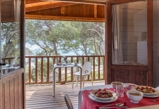 Houten bungalow met zicht op zee en terras, eettafel met maaltijd bij Camping Estival Torre de la Mora.