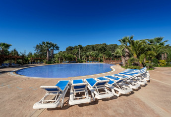 Photo d’un site de glamping avec piscine, transats bleus, palmiers et ciel bleu clair lors d’une journée ensoleillée.