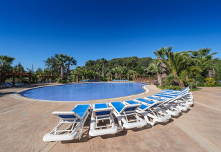 Foto eines Glamping-Resorts mit Pool, Sonnenliegen, Palmen und klarem Himmel an einem schönen Tag.