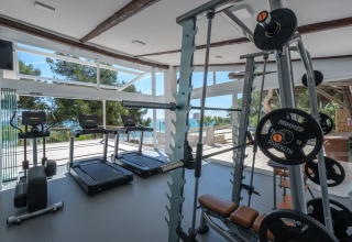Modernes Fitnessstudio mit Laufbändern und Kraftgeräten, große Fenster mit Meer- und Waldblick.