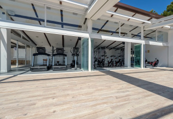 Salle de sport moderne et lumineuse avec tapis de course et vélos, dans un hébergement glamping vitré.