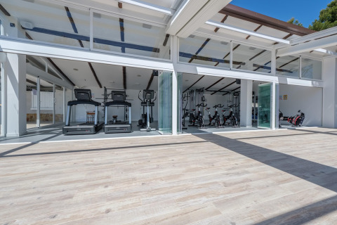 Licht, modern fitnesscentrum met loopbanden en fietsen bij een luxe glampingverblijf met open glazen muren.