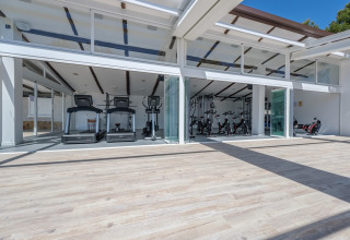 Lyst og moderne fitnesscenter med løbebånd og motionscykler på et luksuriøst glamping-sted med åbne vinduer.