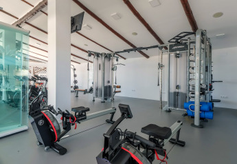 Salle de sport moderne dans un hébergement glamping avec rameurs, station de musculation et lumière naturelle.