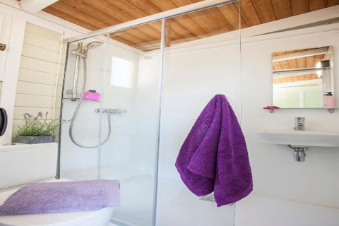 Modernes Badezimmer mit Holzdecke, Glasdusche, lila Handtüchern und weißem Interieur in einer spanischen Hütte.