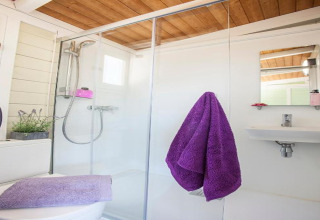 Modern badkamer met houten plafond, glazen douche, paarse handdoeken en wit interieur in Spaanse bungalow.