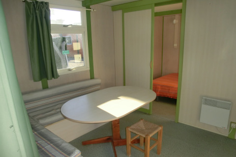 Vista interior del Camping Cambrils Playa 1 Bungalow Oasis con mesa de comedor, banco y dormitorio.