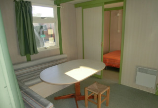 Vista interior del Camping Cambrils Playa 1 Bungalow Oasis con mesa de comedor, banco y dormitorio.