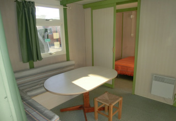Vista interior del Camping Cambrils Playa 1 Bungalow Oasis con mesa de comedor, banco y dormitorio.