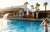 Children having fun at an outdoor pool with a lifeguard at a glamping accommodation with palm trees.