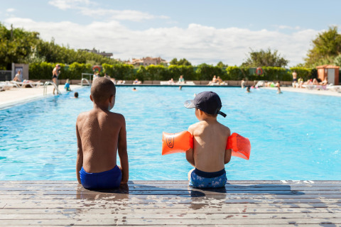Dos niños sentados al borde de la piscina en Camping Cambrils Playa 1 BUNGALOW OASIS en España.