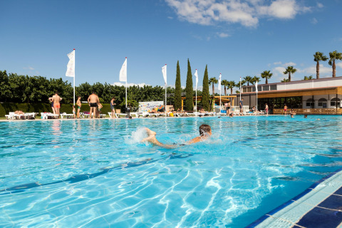 Piscina al aire libre en un alojamiento glamping con huéspedes nadando y tomando el sol bajo cielo azul.