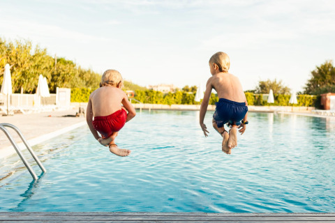 Dos niños con bañadores rojo y azul saltan a la piscina en Camping Cambrils Playa 1 BUNGALOW OASIS, España.