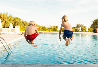 Dos niños con bañadores rojo y azul saltan a la piscina en Camping Cambrils Playa 1 BUNGALOW OASIS, España.