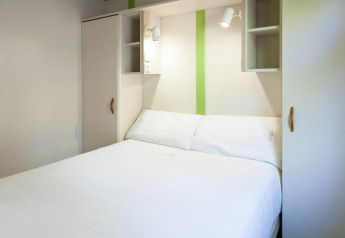 Dormitorio moderno en Camping Cambrils Playa 2 BUNGALOW PREMIUM en España, cama blanca y estanterías.